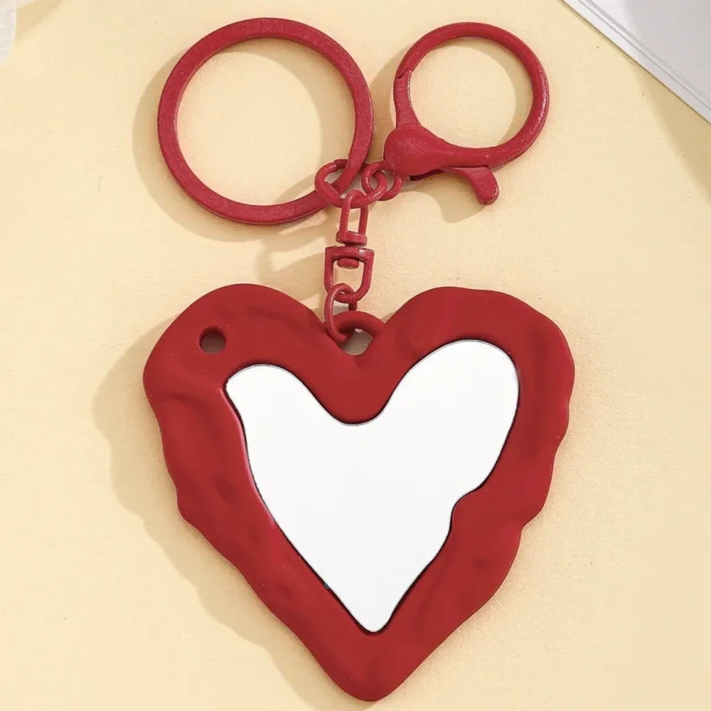 Nine colorful heart-shaped photo frame keychain pendants in purple, pink, hot pink, red, white, black, brown, yellow, and blue with lobster clasp rings on a beige surface. - 8