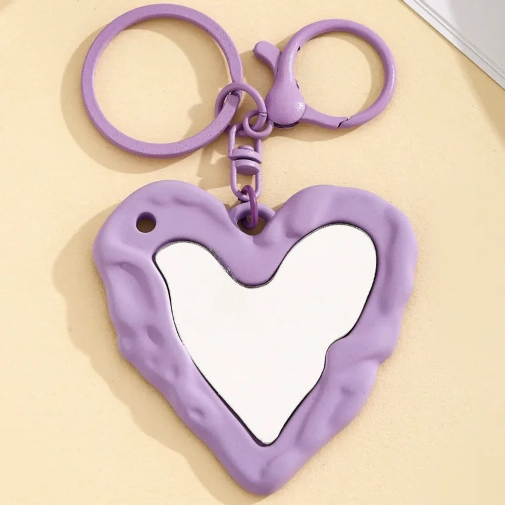 Nine colorful heart-shaped photo frame keychain pendants in purple, pink, hot pink, red, white, black, brown, yellow, and blue with lobster clasp rings on a beige surface. - 9