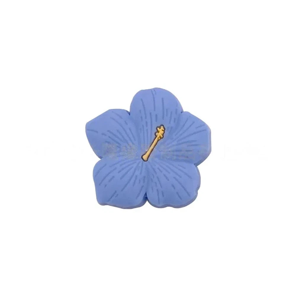 Assorted pastel and earthy tone hibiscus flower silicone focal beads with gold stamen detail displayed on a pink surface, available in colors including blue, purple, green, pink, mauve, brown, tan, yellow, and peach. - Blue