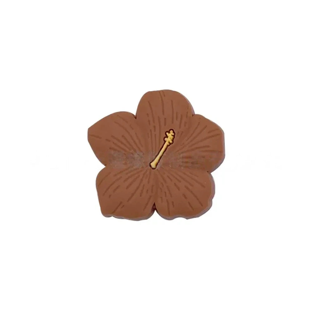 Assorted pastel and earthy tone hibiscus flower silicone focal beads with gold stamen detail displayed on a pink surface, available in colors including blue, purple, green, pink, mauve, brown, tan, yellow, and peach. - Camel