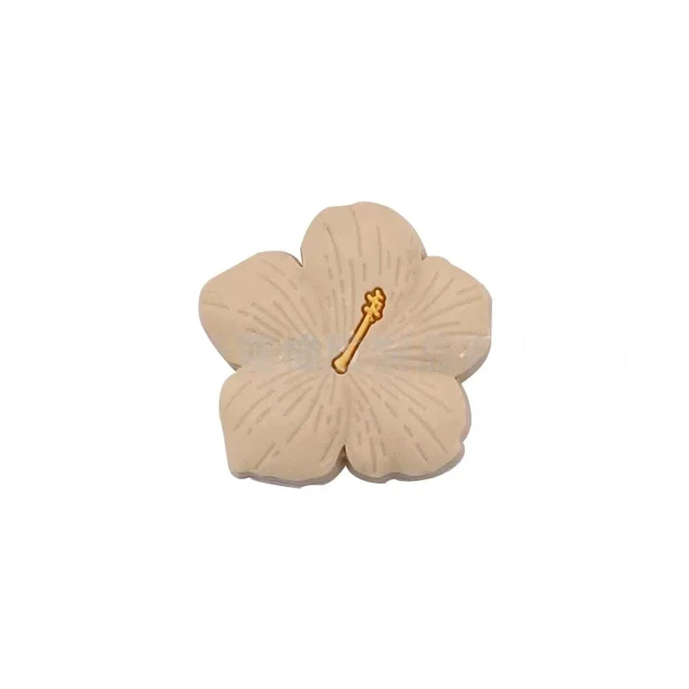 Assorted pastel and earthy tone hibiscus flower silicone focal beads with gold stamen detail displayed on a pink surface, available in colors including blue, purple, green, pink, mauve, brown, tan, yellow, and peach. - Creamy White