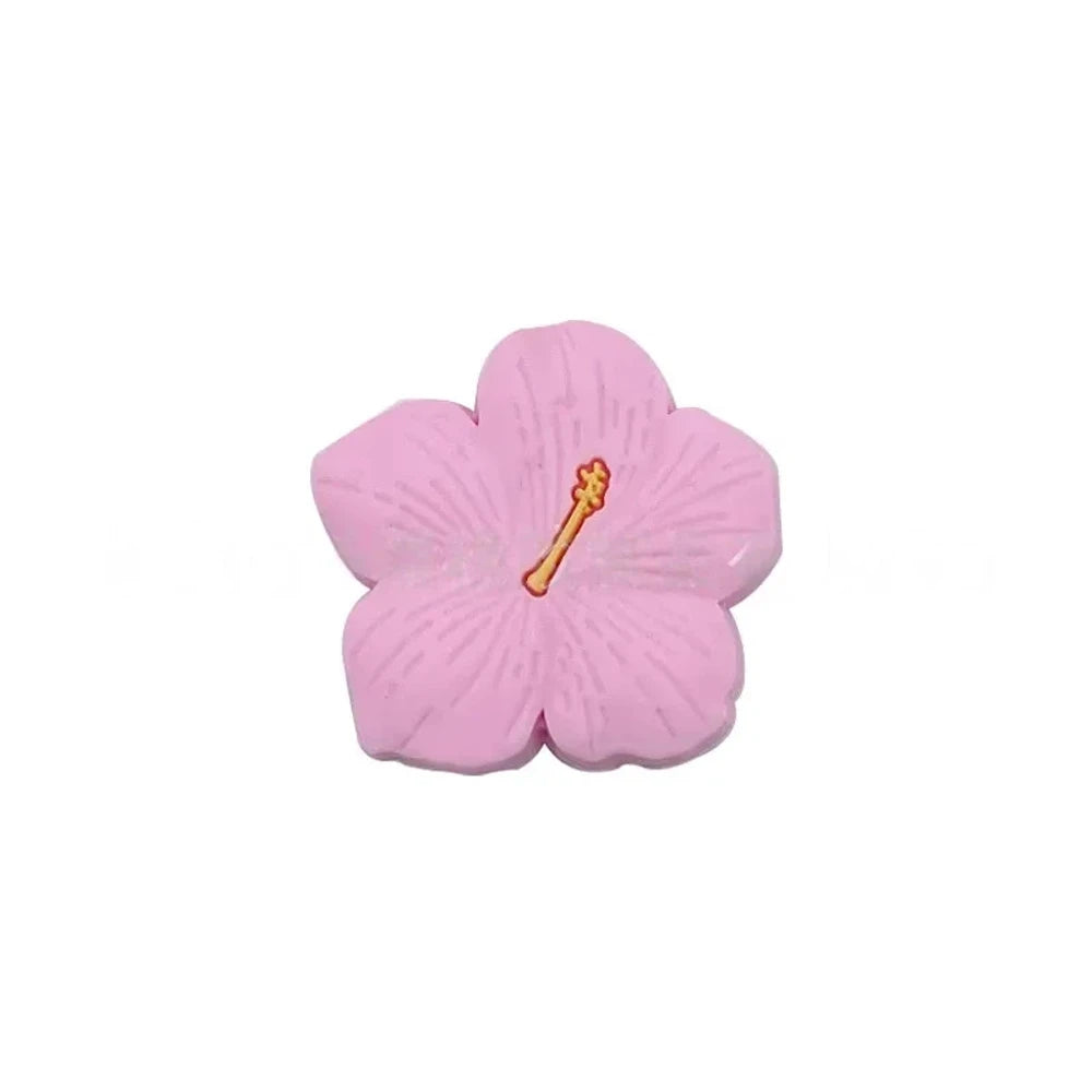 Assorted pastel and earthy tone hibiscus flower silicone focal beads with gold stamen detail displayed on a pink surface, available in colors including blue, purple, green, pink, mauve, brown, tan, yellow, and peach. - Light Pink