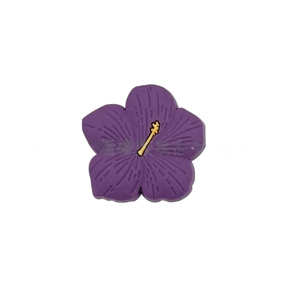 Assorted pastel and earthy tone hibiscus flower silicone focal beads with gold stamen detail displayed on a pink surface, available in colors including blue, purple, green, pink, mauve, brown, tan, yellow, and peach. - Purple