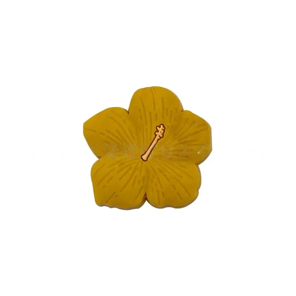 Assorted pastel and earthy tone hibiscus flower silicone focal beads with gold stamen detail displayed on a pink surface, available in colors including blue, purple, green, pink, mauve, brown, tan, yellow, and peach. - Yellow