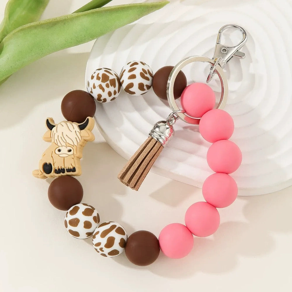 Silicone bead bracelet keychains featuring highland cow charms, cow print beads, and solid pink and blue silicone beads with tassel accents. - Blue