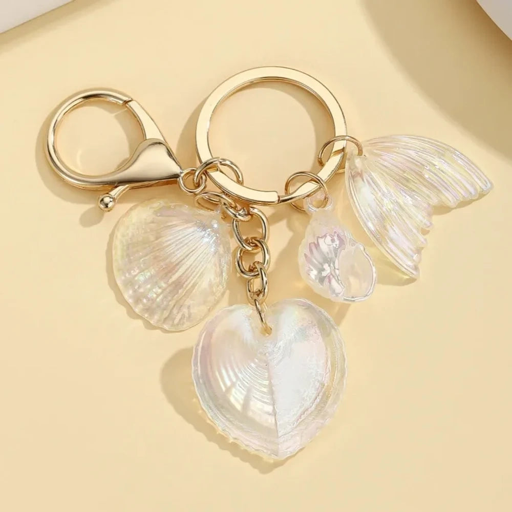 Five iridescent pastel resin keychain charms featuring heart-shaped shells, scallop shells, and mermaid tail pendants on gold lobster clasp key rings in blue, pink, and purple tones. - 1