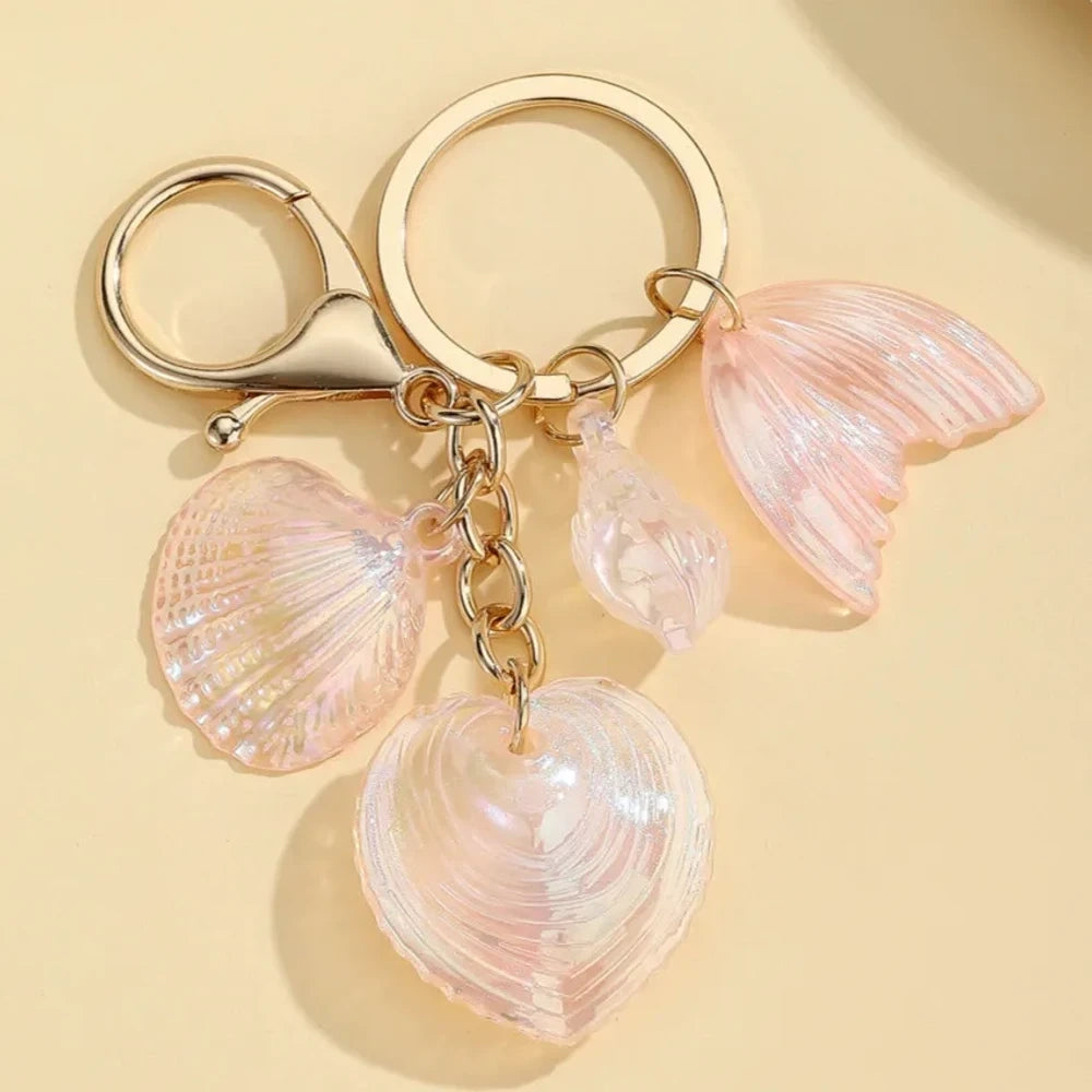 Five iridescent pastel resin keychain charms featuring heart-shaped shells, scallop shells, and mermaid tail pendants on gold lobster clasp key rings in blue, pink, and purple tones. - 2