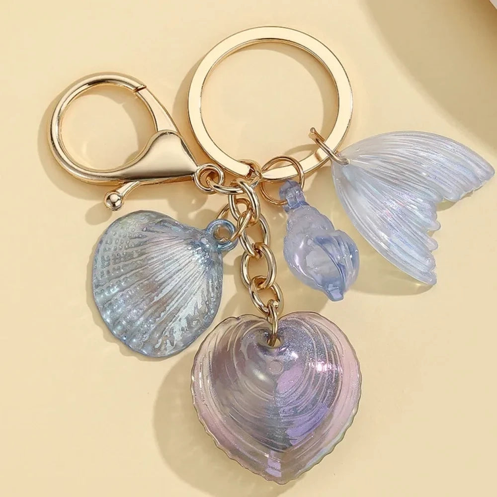 Five iridescent pastel resin keychain charms featuring heart-shaped shells, scallop shells, and mermaid tail pendants on gold lobster clasp key rings in blue, pink, and purple tones. - 3