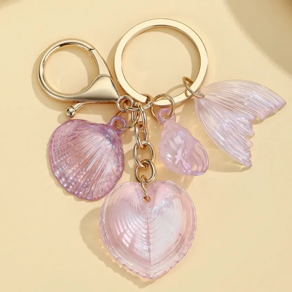 Five iridescent pastel resin keychain charms featuring heart-shaped shells, scallop shells, and mermaid tail pendants on gold lobster clasp key rings in blue, pink, and purple tones. - 5