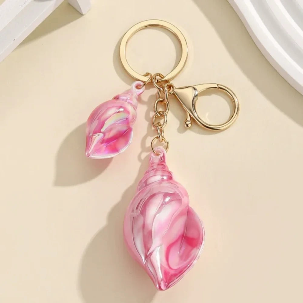 Six colorful iridescent swirl resin conch shell keychain charms in rainbow, pink, blue, white, and purple with gold lobster clasp hardware on a cream background. - Pink