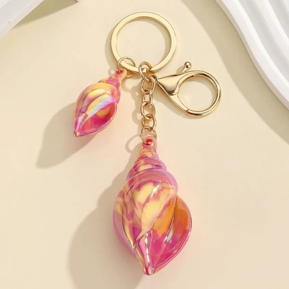 Six colorful iridescent swirl resin conch shell keychain charms in rainbow, pink, blue, white, and purple with gold lobster clasp hardware on a cream background. - Red