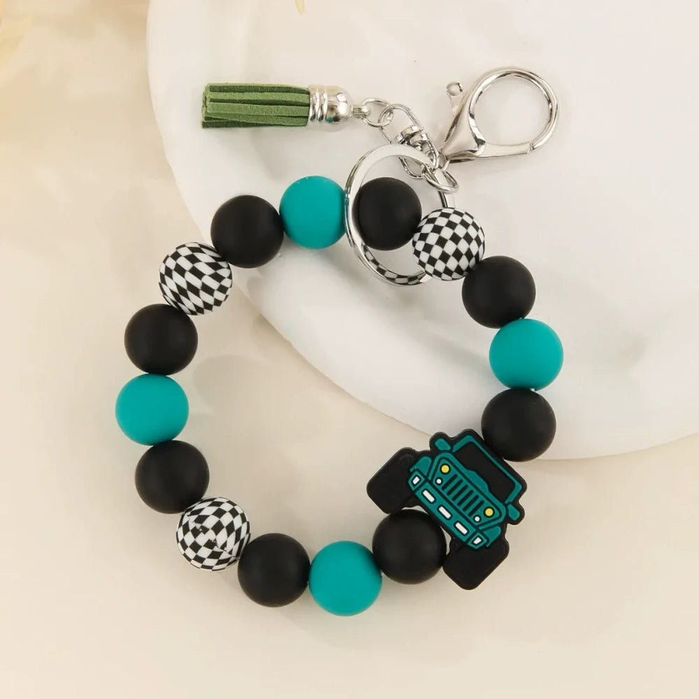 Four beaded bracelet keychains featuring jeep car silicone beads in red, teal, blue, and yellow with black and checkered beads and tassel accents on a white surface. - Green