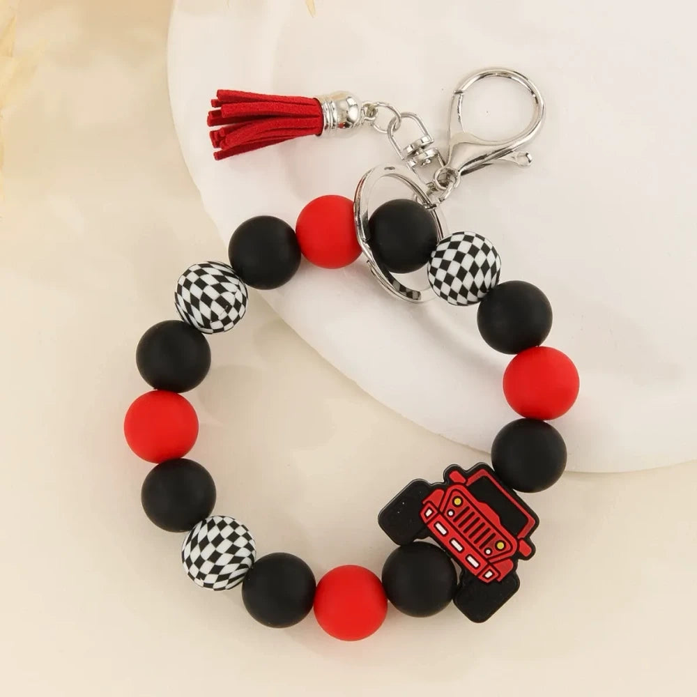 Four beaded bracelet keychains featuring jeep car silicone beads in red, teal, blue, and yellow with black and checkered beads and tassel accents on a white surface. - Red