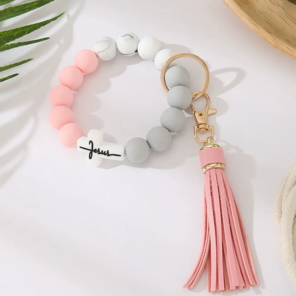 Four Jesus cross silicone bead bracelet keychains with leather tassels in beige, pink, blue, and gray marble color combinations on a white surface. - 4