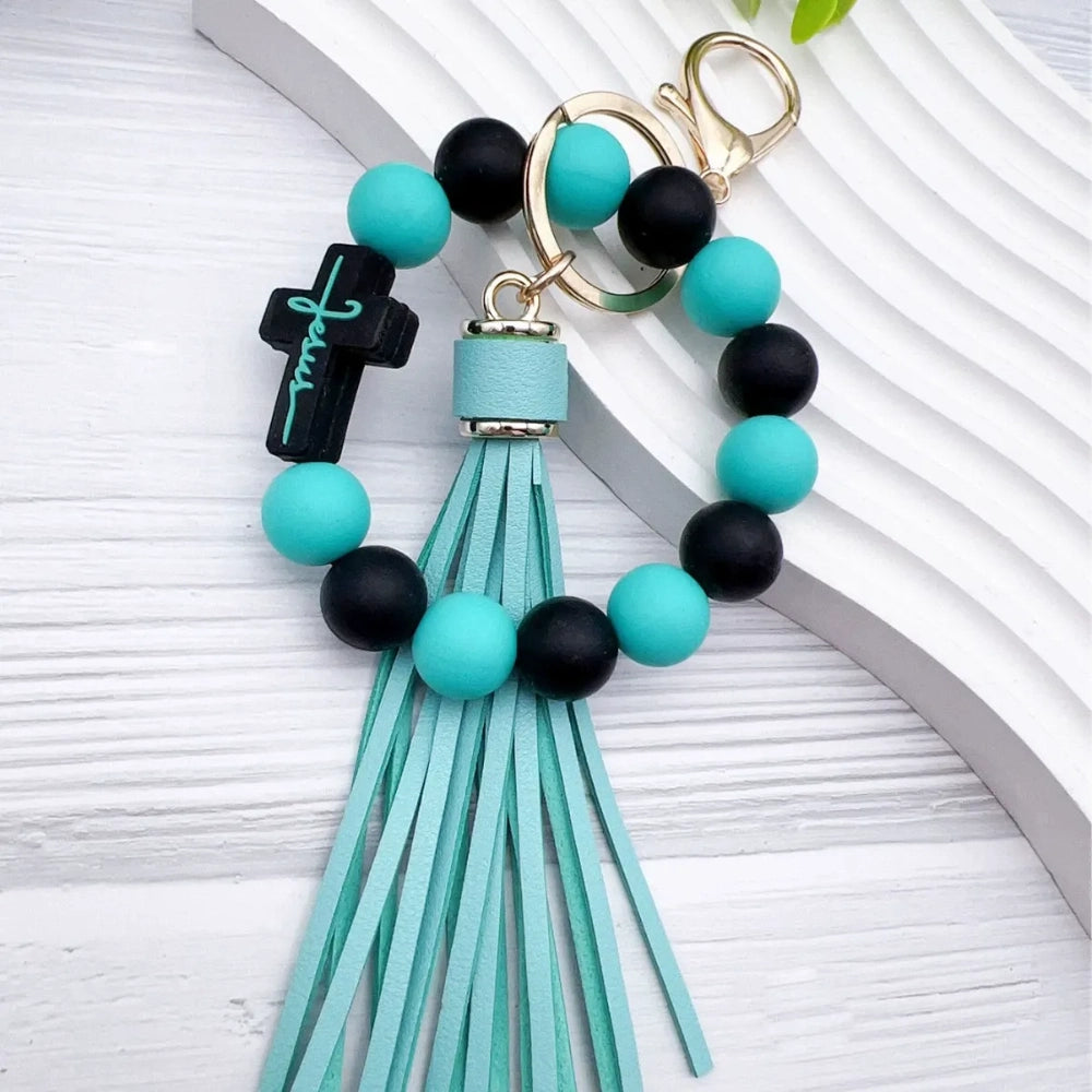 Colorful Jesus cross silicone bead stretch bracelets with tassel keychains in black, pink, purple, teal, and green color combinations on white background. - Blue