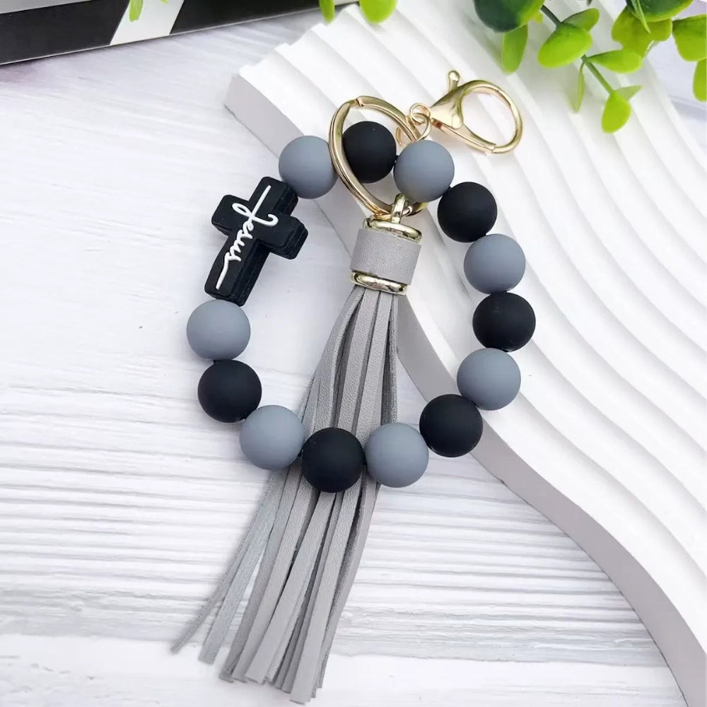 Colorful Jesus cross silicone bead stretch bracelets with tassel keychains in black, pink, purple, teal, and green color combinations on white background. - Gray