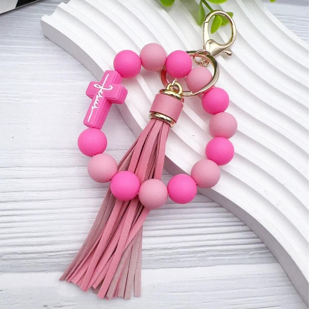 Colorful Jesus cross silicone bead stretch bracelets with tassel keychains in black, pink, purple, teal, and green color combinations on white background. - Pink-1