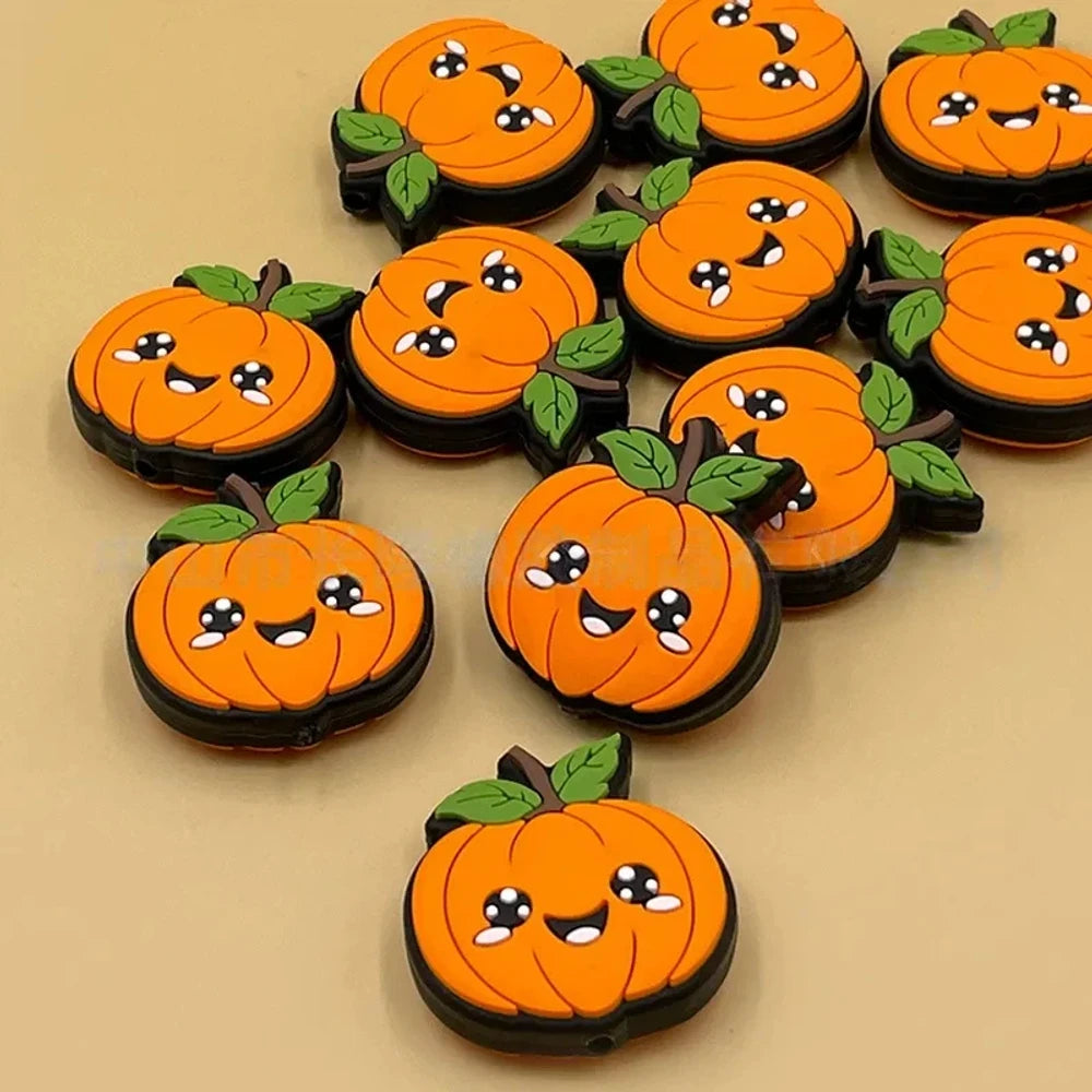 Kawaii smiling orange pumpkin silicone focal beads with green leaves and black outline, shown in a group on a tan background, perfect for Halloween beadable pens and keychains.