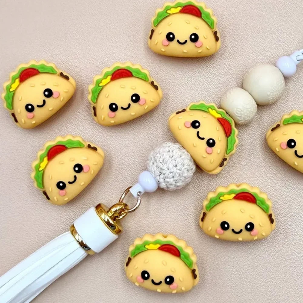 Kawaii smiley face taco silicone focal beads displayed with a beadable pen and white tassel on a beige background, perfect for DIY crafting projects.