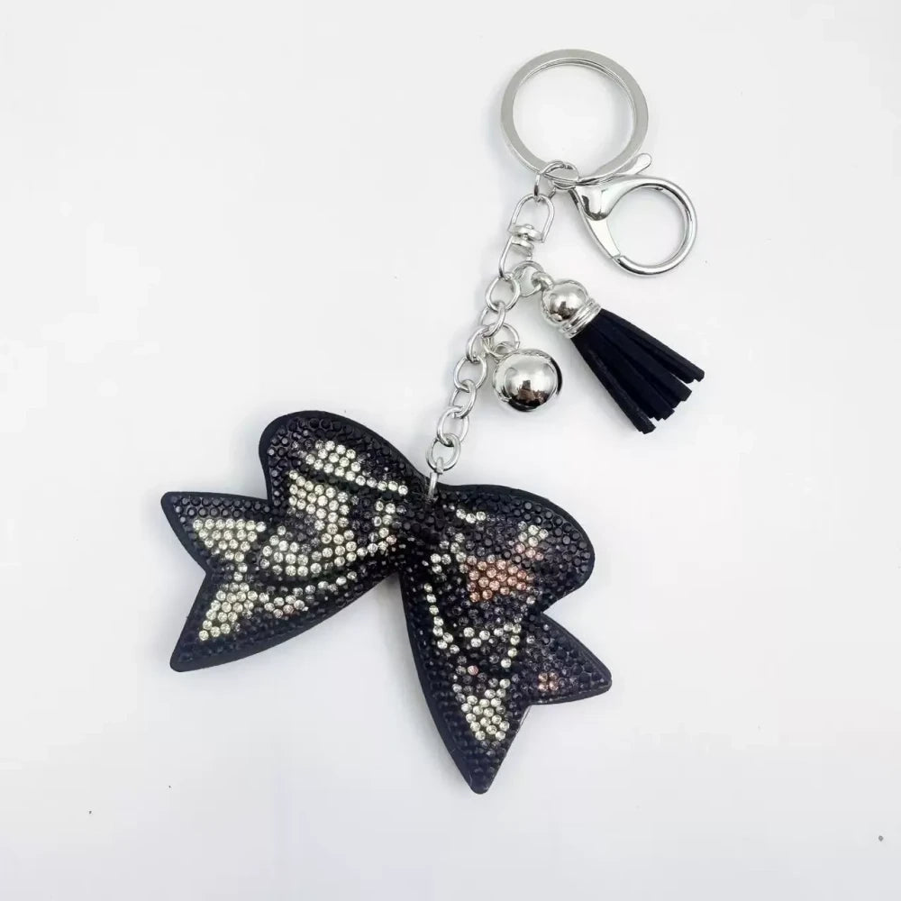 Large black bow-shaped fancy bead with AB rhinestone sparkle, shown styled as decorative keychain charms with tassels and silver hardware. - 1