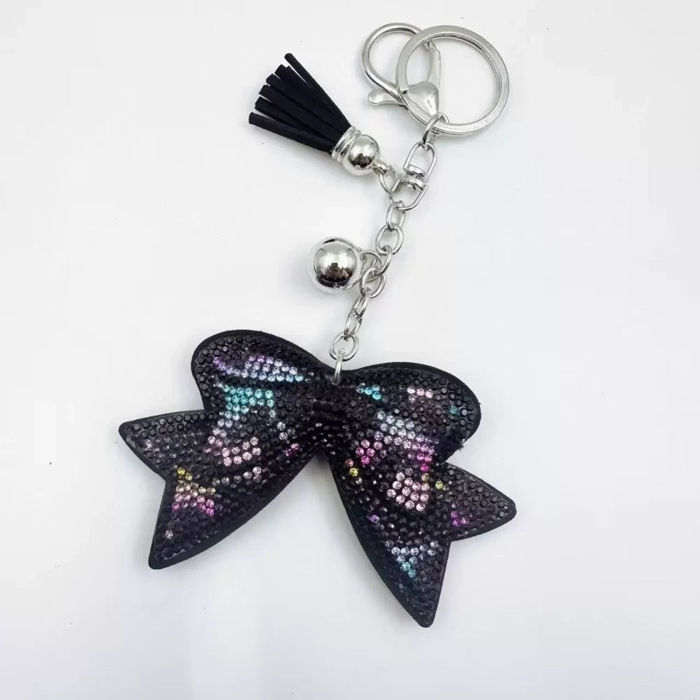 Large black bow-shaped fancy bead with AB rhinestone sparkle, shown styled as decorative keychain charms with tassels and silver hardware. - 6