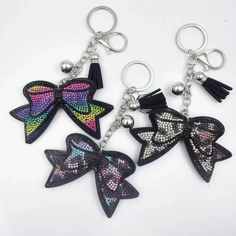 Large black bow-shaped fancy bead with AB rhinestone sparkle, shown styled as decorative keychain charms with tassels and silver hardware. - Random Mixed