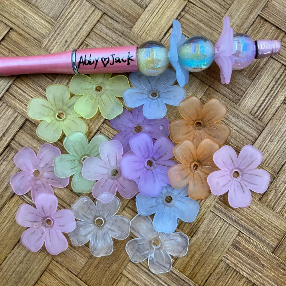 Mixed pastel frosted flower acrylic spacer beads with center holes displayed next to a pink beadable pen