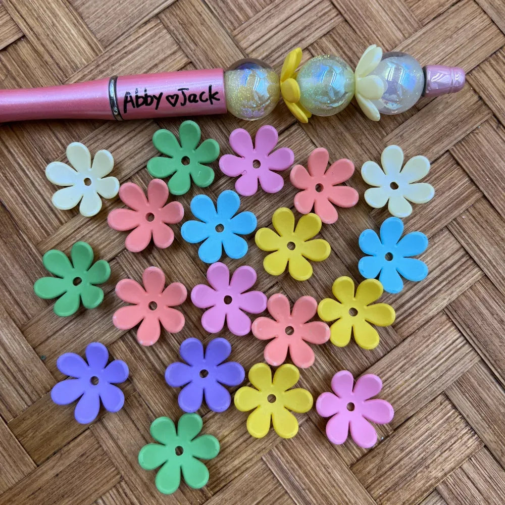 Large mixed pastel daisy acrylic spacer beads with center holes displayed beside a pink decorated beadable pen