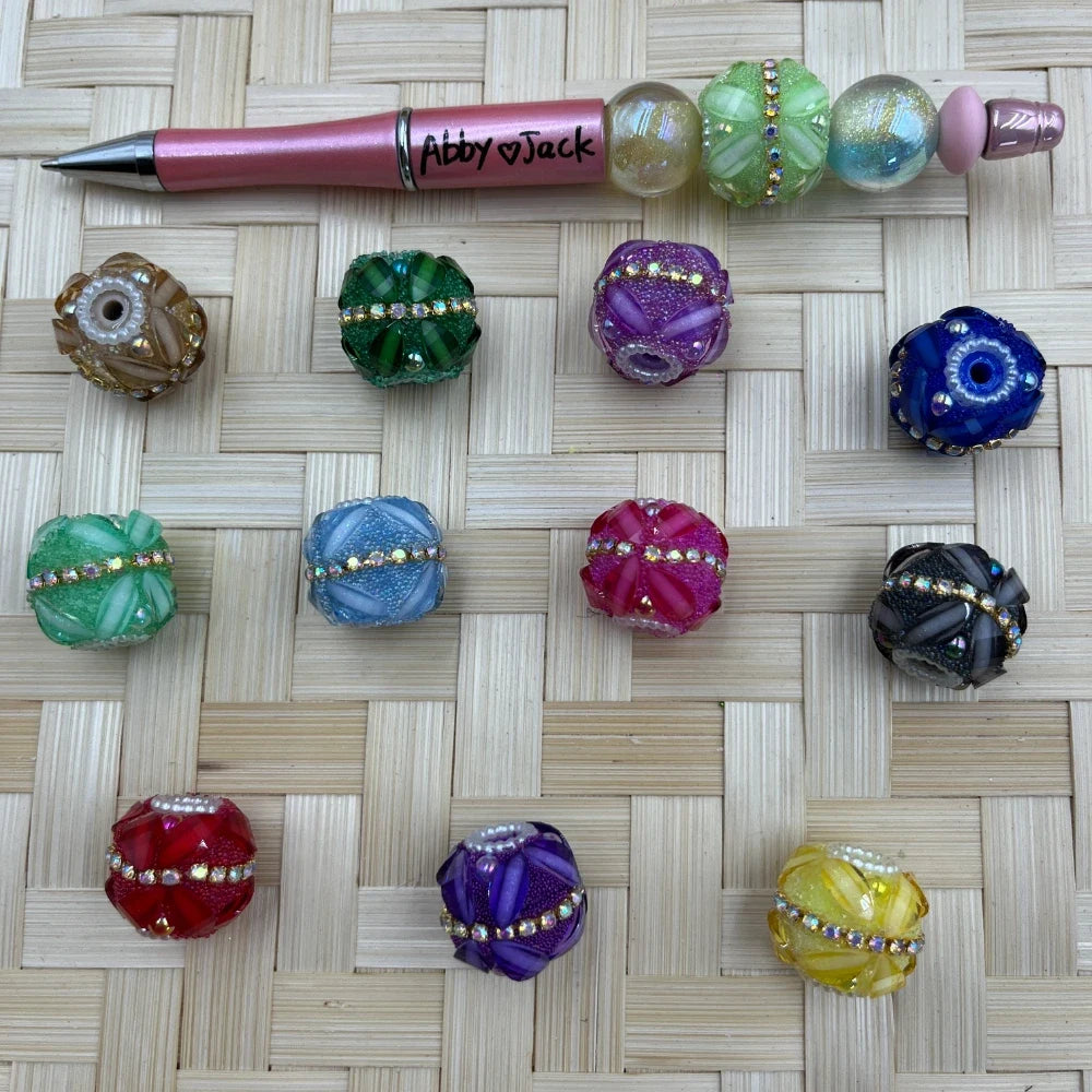 Assorted colorful floral rhinestone glass fancy beads with a beadable pen sample on a woven mat