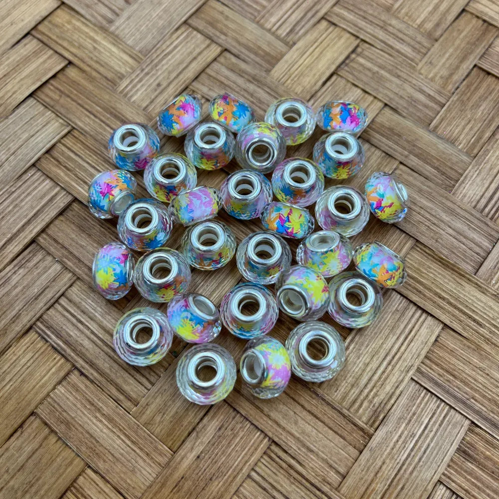 Clear large hole acrylic spacer beads with a rainbow paint splatter pattern on a wood surface
