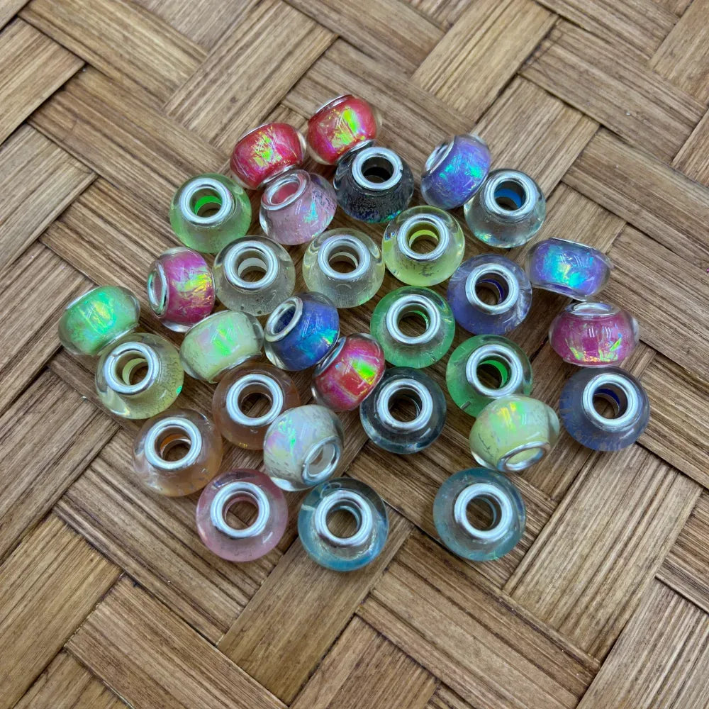 Mixed pastel iridescent acrylic spacer beads with large silver-tone center holes on a woven wood background