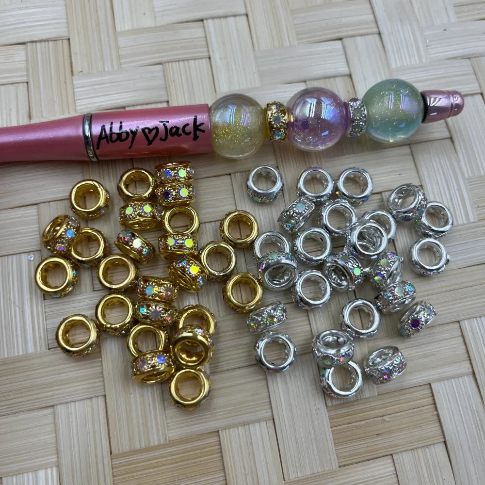 Gold and silver large-hole metal spacer beads with AB rhinestone inlay displayed beside a decorated beadable pen.