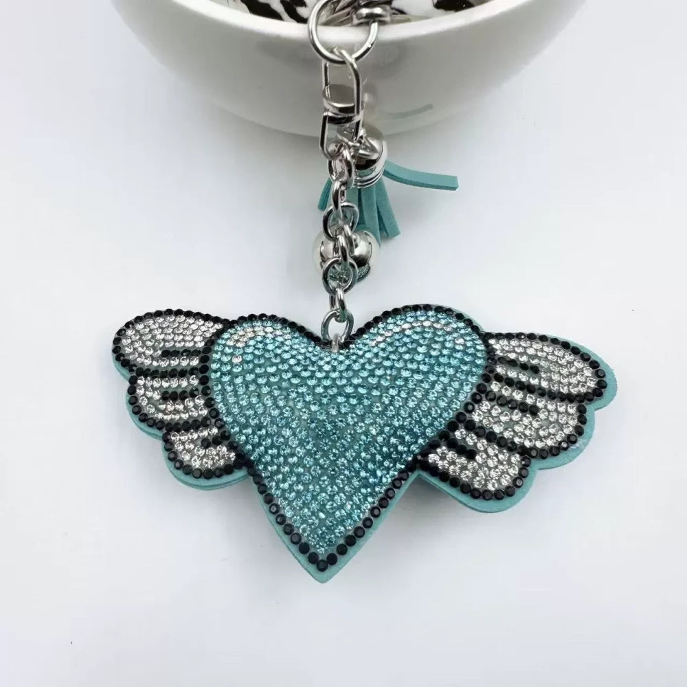 Purple and pink winged heart rhinestone charm beads with tassels, bells, and silver key rings on a white background - Blue