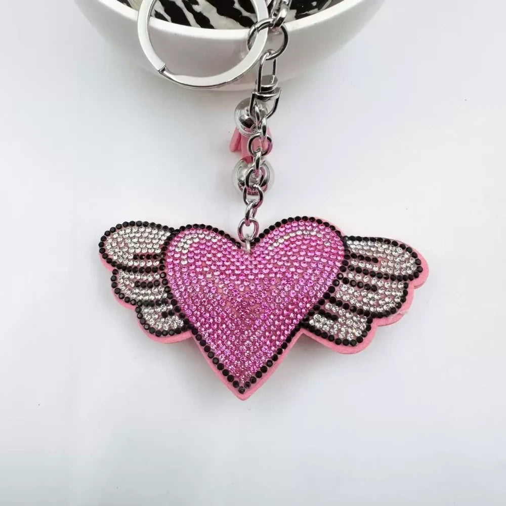 Purple and pink winged heart rhinestone charm beads with tassels, bells, and silver key rings on a white background - Pink