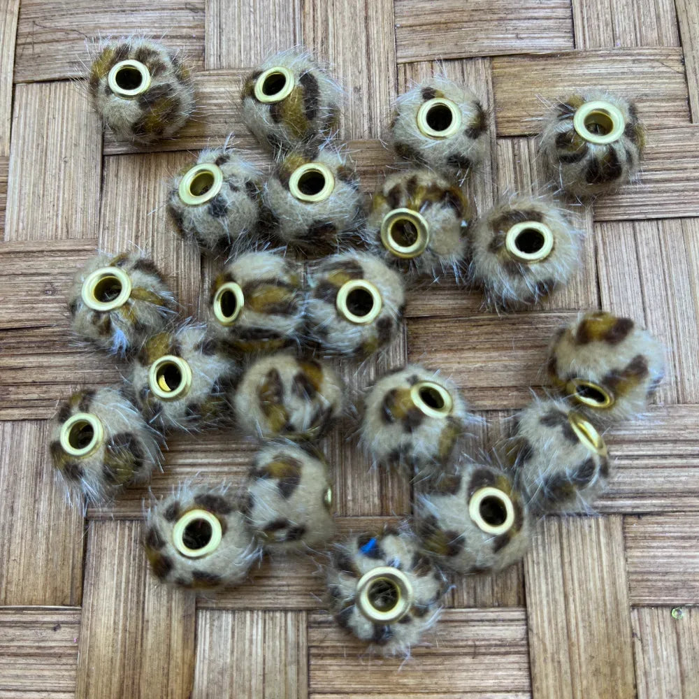 Close-up of leopard print faux fur furry spacer beads with gold metal rings on a woven bamboo surface, used for beadable pens, keychains, and DIY jewelry making.