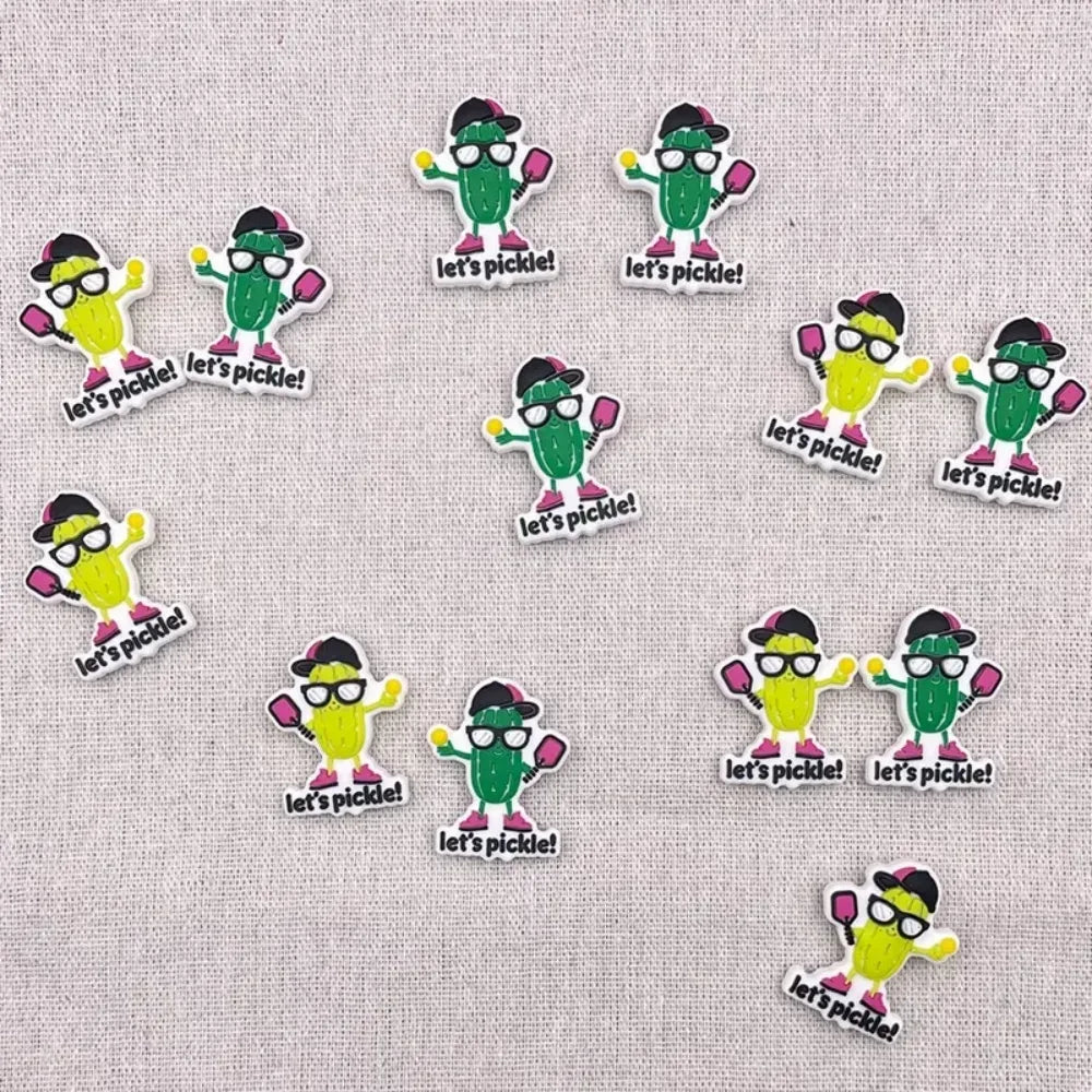 Silicone focal beads featuring a cartoon pickle character wearing glasses and a black cap holding a pickleball paddle with 'Let's Pickle!' text, shown in multiple sizes on a linen background.