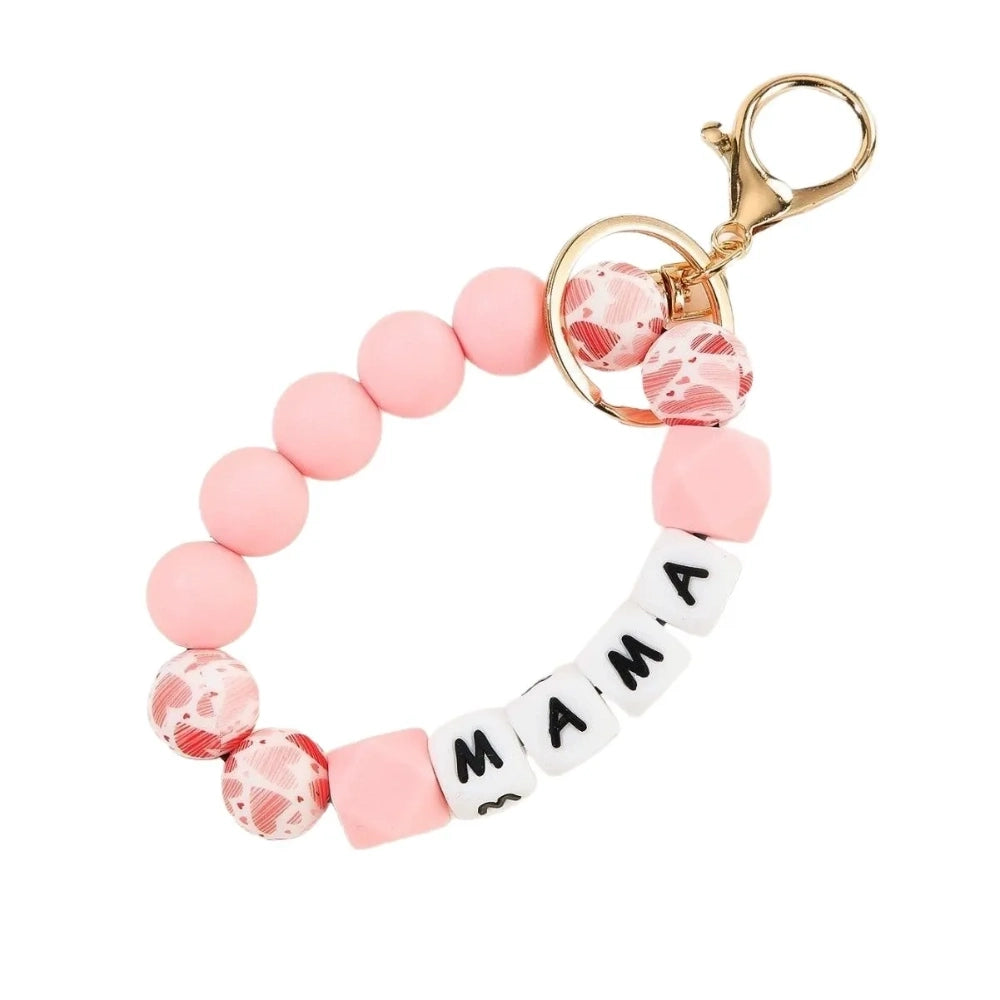 Seven MAMA letter silicone bead wristlet keychains in assorted colors including mint, lavender, gray, yellow, pink, black, and green with patterned accent beads and gold lobster clasp hardware on a light background. - Pink