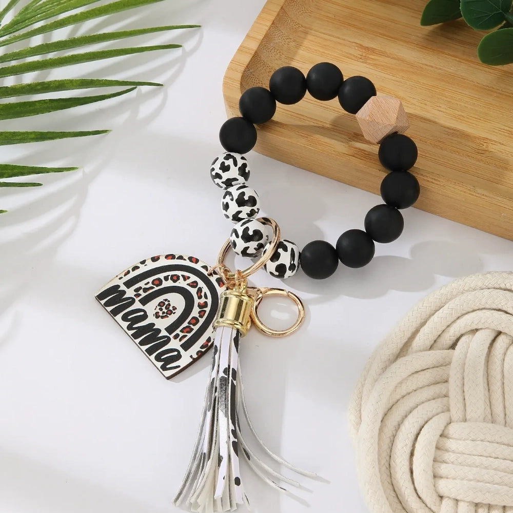 Set of 8 Mama rainbow leopard print silicone bead wristlet keychains with leather tassels and heart charm pendants in assorted colors including black, blue, yellow, green, pink, red, and purple on white background. - Black