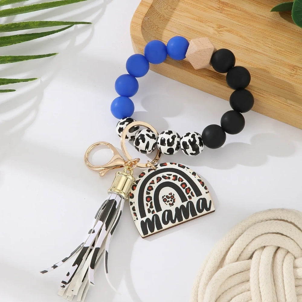 Set of 8 Mama rainbow leopard print silicone bead wristlet keychains with leather tassels and heart charm pendants in assorted colors including black, blue, yellow, green, pink, red, and purple on white background. - Blue