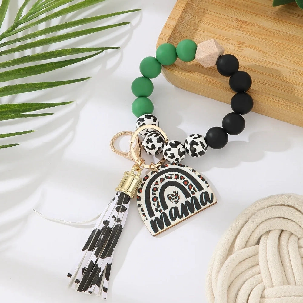 Set of 8 Mama rainbow leopard print silicone bead wristlet keychains with leather tassels and heart charm pendants in assorted colors including black, blue, yellow, green, pink, red, and purple on white background. - Green