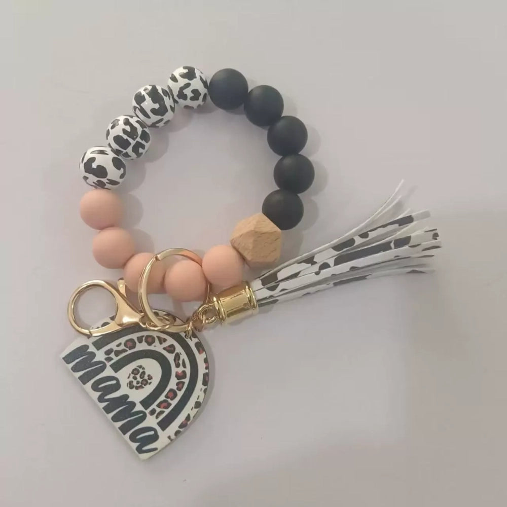 Set of 8 Mama rainbow leopard print silicone bead wristlet keychains with leather tassels and heart charm pendants in assorted colors including black, blue, yellow, green, pink, red, and purple on white background. - Pink