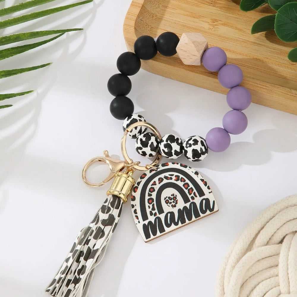Set of 8 Mama rainbow leopard print silicone bead wristlet keychains with leather tassels and heart charm pendants in assorted colors including black, blue, yellow, green, pink, red, and purple on white background. - Purple