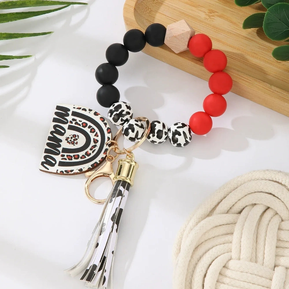 Set of 8 Mama rainbow leopard print silicone bead wristlet keychains with leather tassels and heart charm pendants in assorted colors including black, blue, yellow, green, pink, red, and purple on white background. - Red