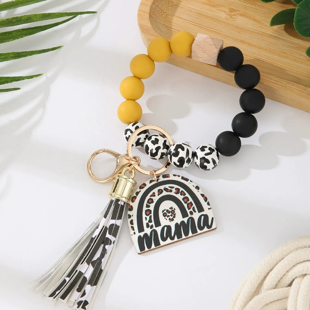 Set of 8 Mama rainbow leopard print silicone bead wristlet keychains with leather tassels and heart charm pendants in assorted colors including black, blue, yellow, green, pink, red, and purple on white background. - Yellow