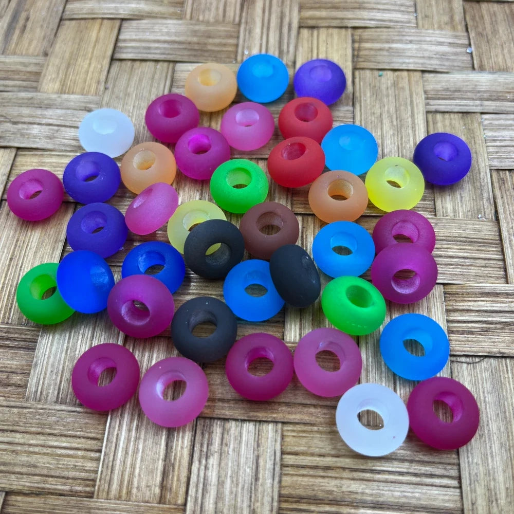 Assorted matte frosted multicolor acrylic spacer beads in pink, purple, blue, green, orange, yellow, red, black and white with large center holes on a woven bamboo surface