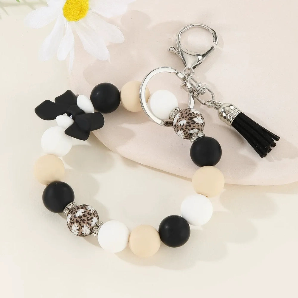 Set of colorful silicone bead stretch bracelet keychains in pastel and bold colors including pink, blue, green, yellow, purple, teal, and black, each featuring a lobster clasp, decorative printed silicone bead, tassel or bow accent, displayed on a white surface. - Black