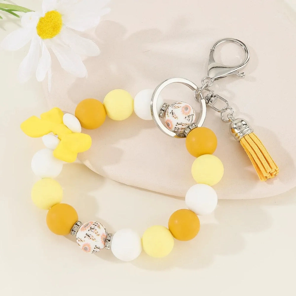 Set of colorful silicone bead stretch bracelet keychains in pastel and bold colors including pink, blue, green, yellow, purple, teal, and black, each featuring a lobster clasp, decorative printed silicone bead, tassel or bow accent, displayed on a white surface. - Yellow