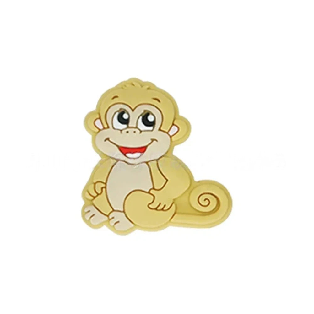 Seven colorful cartoon monkey silicone focal beads in brown, tan, grey, yellow, pink, blue, and purple displayed on a miniature white bench against a pink background. - Brown