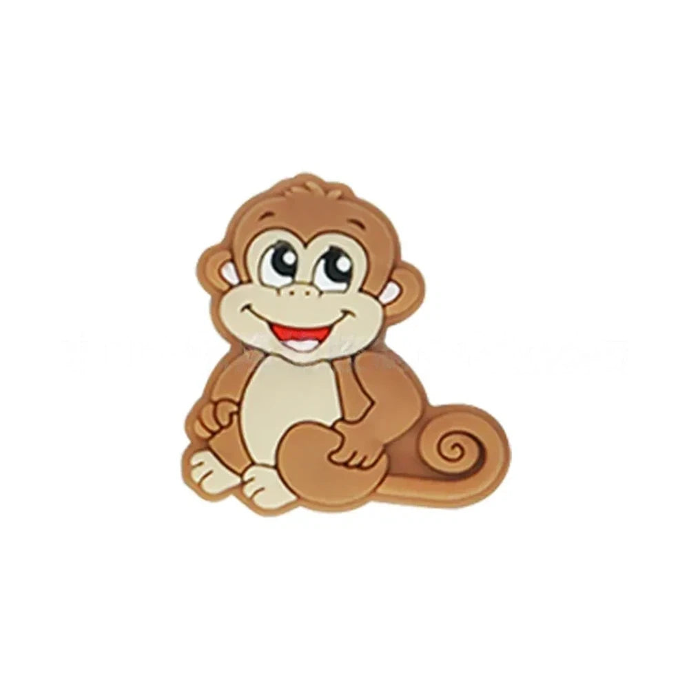Seven colorful cartoon monkey silicone focal beads in brown, tan, grey, yellow, pink, blue, and purple displayed on a miniature white bench against a pink background. - Camel