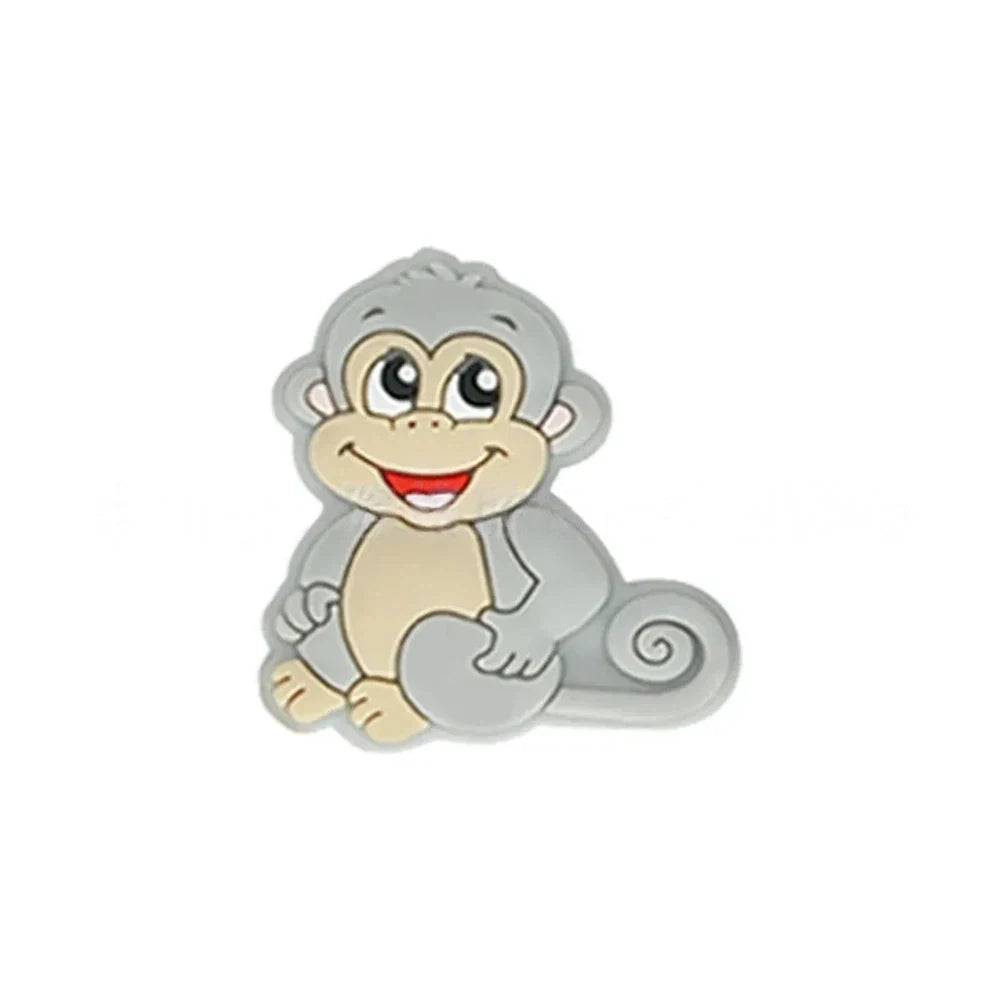 Seven colorful cartoon monkey silicone focal beads in brown, tan, grey, yellow, pink, blue, and purple displayed on a miniature white bench against a pink background. - Light Gray